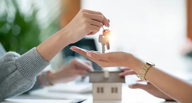 Mãos de uma mulher entregando as chaves para outra, simbolizando a concretização de um negócio no mercado imobiliário.